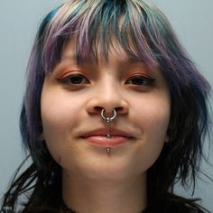 a woman with blue and purple hair has a nose ring on her nose while wearing piercings