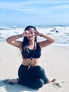 a woman sitting on the beach with her hands behind her head