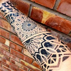 a man's arm with an intricate tattoo design on it, next to a brick wall