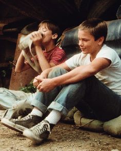 two young boys sitting on the ground with their skateboards in front of them and one boy holding his hand up to his mouth