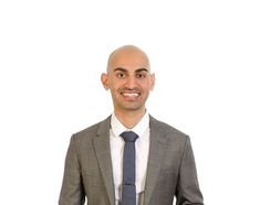 a man in a suit and tie smiling at the camera with his hands on his hips