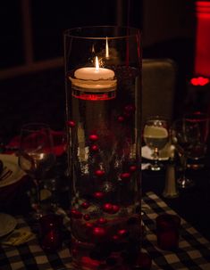 a candle is lit in a glass vase filled with water and red balls on the table