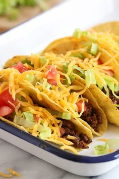 three tacos on a plate with cheese and lettuce