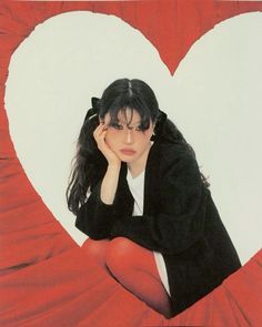 a woman sitting on top of a red heart shaped pillow with her hands to her face