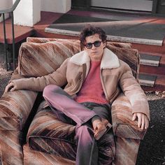 a man sitting on top of a couch wearing sunglasses and a coat with a fur collar