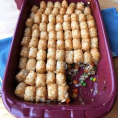 a purple dish filled with tater tots on top of a wooden table