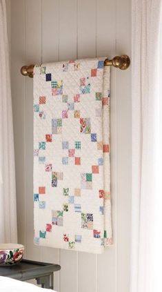 a white quilt hanging on the wall next to a table with a plate and bowl