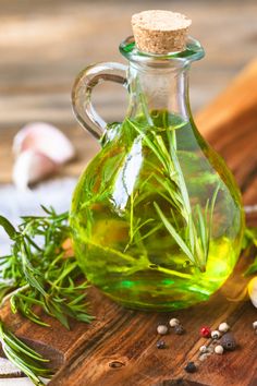 a bottle filled with green liquid sitting on top of a wooden cutting board next to garlic