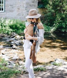 a woman in white pants and a hat holding a baby