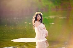 a pregnant woman sitting on top of a body of water wearing a flower crown while holding her belly