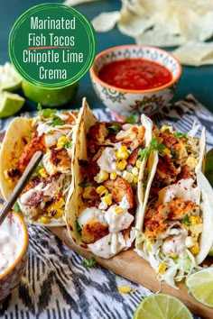 three fish tacos on a cutting board with limes and salsa in the background