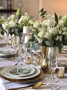 the table is set with white flowers and gold place settings for an elegant dinner party