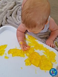 a baby is playing with yellow food on the floor in front of a white tray