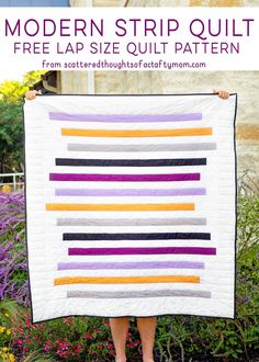 a woman holding up a modern strip quilt in front of some flowers and bushes with the text, modern strip quilt free lap size quilt pattern