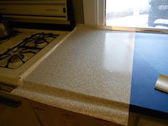 a kitchen counter with a stove top next to a window and an oven in the background