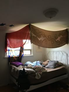 an unmade bed sitting under a window in a bedroom