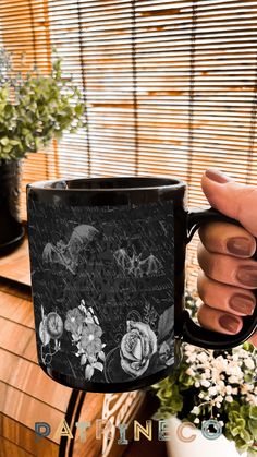 a hand holding a black coffee mug with flowers on it and an image of horses in the background