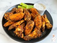 chicken wings with celery and ranch dressing on a black plate next to a small bowl of ranch dressing