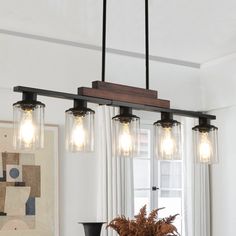 three lights hanging over a dining table in a room with white walls and curtains on the windowsill