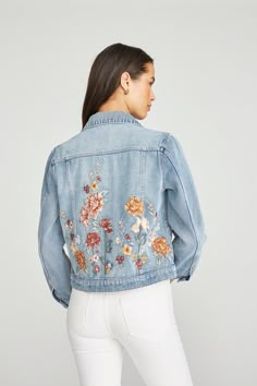 a woman wearing a jean jacket with floral embroidered on the front and back, facing forward