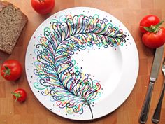 a white plate topped with a colorful peacock feather next to sliced tomatoes and a slice of bread