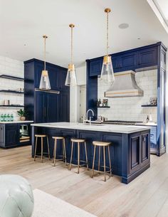 a large kitchen with blue cabinets and white marble counter tops, gold pendant lights over the island