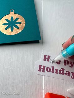 someone is writing on a holiday card with a blue marker and some other crafting supplies