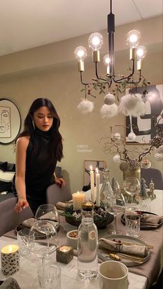 a woman standing in front of a dining room table with candles and dishes on it