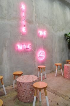 several stools and tables in front of a wall with pink neon signs on it