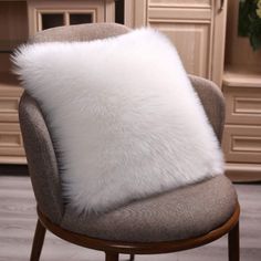 a white fur pillow sitting on top of a chair next to a wooden table and dresser