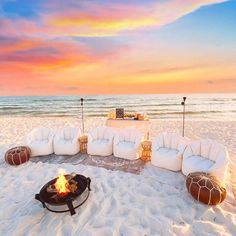 a fire pit on the beach with chairs around it