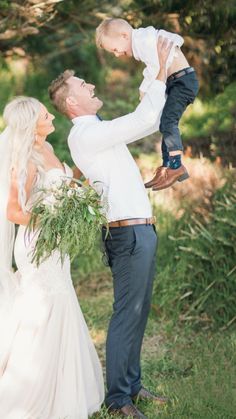 a man holding a baby in his arms while standing next to a woman wearing a wedding dress