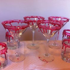 there are many wine glasses on the table with red liquid pouring out of them to make it look like they're dripping