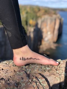 a person's foot with a small tattoo on the side of their foot, overlooking water