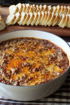 a casserole dish with meat and cheese in it on a table next to bread