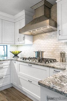 a kitchen with white cabinets and marble counter tops, an oven hood over the stove