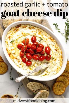 a bowl of dip with cherry tomatoes and crackers on the side next to bread