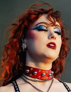 a woman with red hair and blue eyes wearing choker, necklaces and piercings