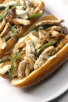 two sandwiches on a white plate with green peppers and mushrooms in the middle, sitting side by side