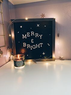 a lighted merry and bright sign sitting on top of a white table next to a lit candle