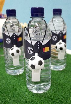 three plastic water bottles with soccer themed labels on them sitting on green grass next to a blue wall