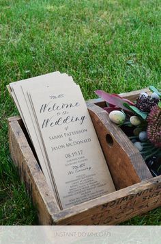 a wooden box filled with wedding programs on top of green grass next to flowers and greenery