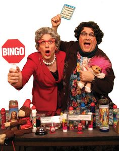 two people standing behind a table holding up signs and stuffed animals in front of them