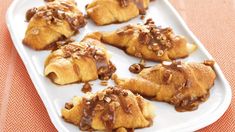 a white plate topped with pastries covered in chocolate and pecans on an orange table cloth