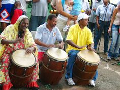 two men sitting on the ground playing drums in front of people standing and watching them