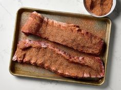 two pieces of meat sitting on top of a baking pan next to some seasoning