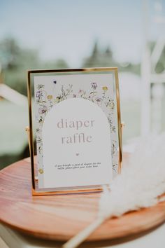 a sign that says diaper raffle on top of a wooden table next to a white feather