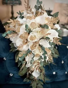 a bridal bouquet with white flowers and greenery on a blue velvet couch in a living room