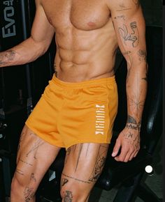 a shirtless man sitting in a chair with tattoos on his arms and legs, wearing yellow shorts