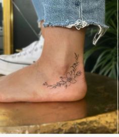 a woman's foot with a small flower tattoo on the side of her ankle